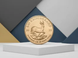 Goldrausch per Mausklick: Mein Experiment mit dem 1/10 Unze Krügerrand von Amazon Eine südafrikanische 1/10-Unzen-Goldmünze Krugerrand aus dem Jahr 2021, die auf einem weißen Podest vor einem abstrakten geometrischen Hintergrund in Blau, Grau und Gold präsentiert wird. Die Münze zeigt das Motiv einer Springbock-Antilope.