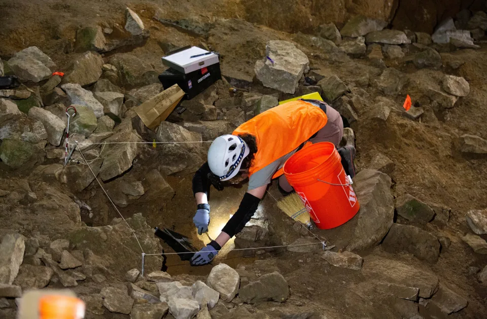 Kailey Alessi von der University of Idaho bürstet einen Teil der Erde, während sie mit einem Team von Archäologen an einer archäologischen Ausgrabung in der natürlichen vertikalen Grube arbeitet.