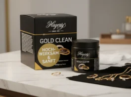Hagerty Gold Clean im Test: Der Wellness-Urlaub für Ihren Goldschmuck A professional display of Hagerty Gold Clean jewelry cleaning products, featuring a black box and jar alongside several gold rings and a necklace resting on a black polishing cloth atop a marble surface.